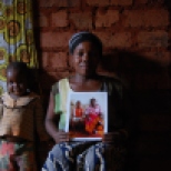 Jackie Niyonzima, 27, and her son Elias Vyizigiro, 5, pose with a picture of her oldest son and her mother who now live in Chattanooga. Money that Jackie's mother sent back to Burundi helped build this small mud house.